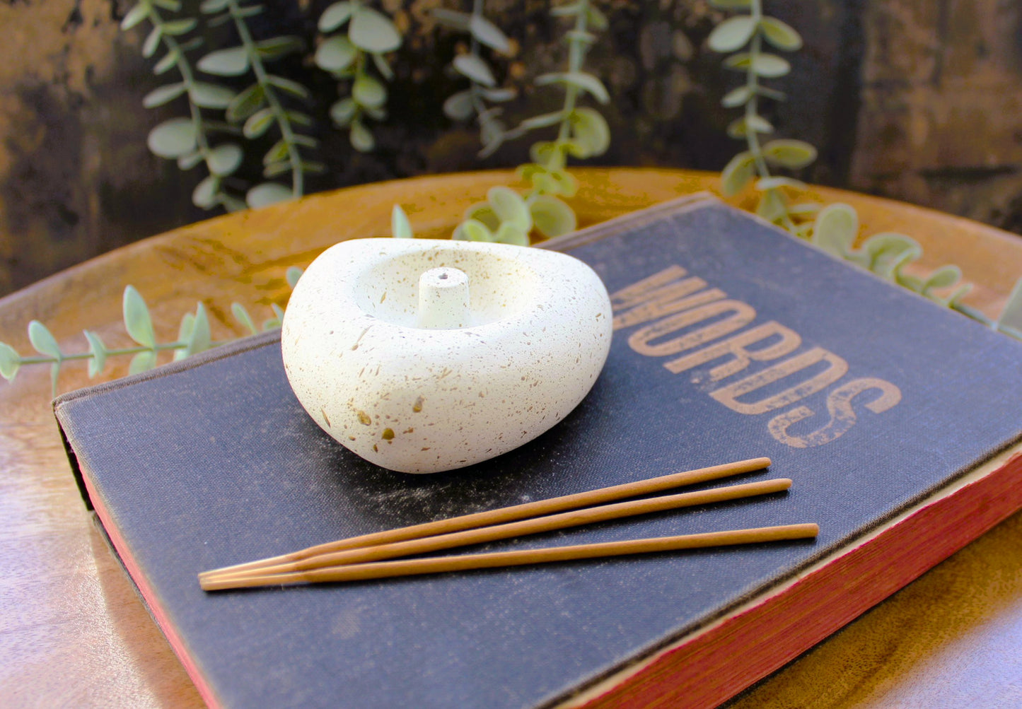 Antique white heart shaped incense holder sitting upon an old book with 3 incense sticks in the foreground