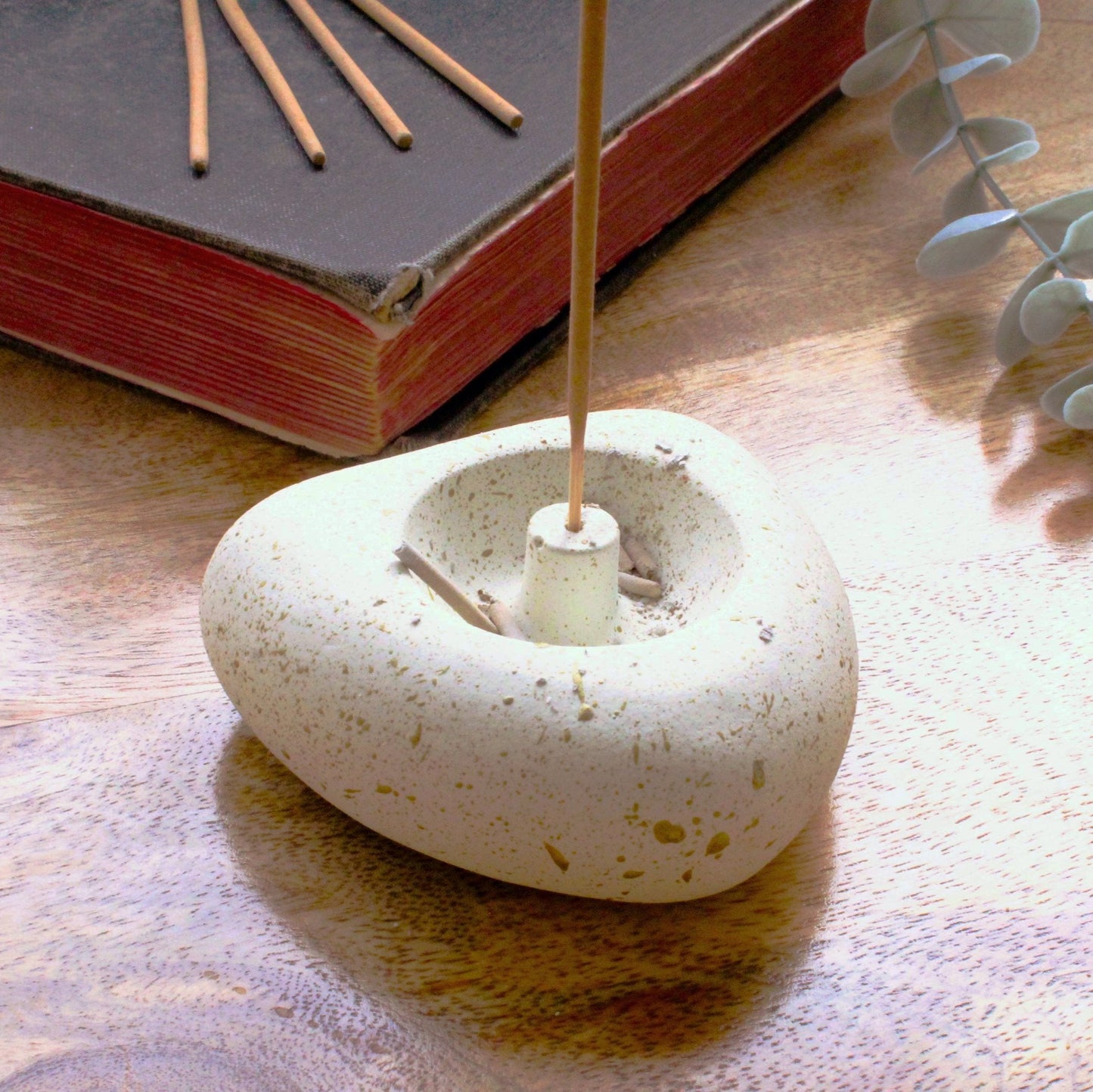Antique white heart shaped incense stick holder sitting on a wooden surface with an old book in the background. 4 incense stick sit on the book