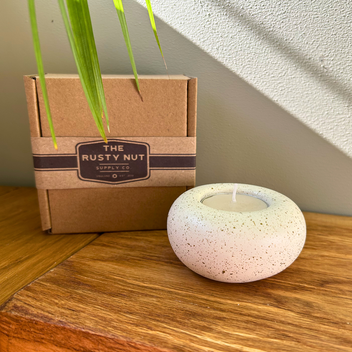 Cast stone Sanctuary tealight holder with lit tealight displayed beside The Rusty Nut Supply Co branded gift box