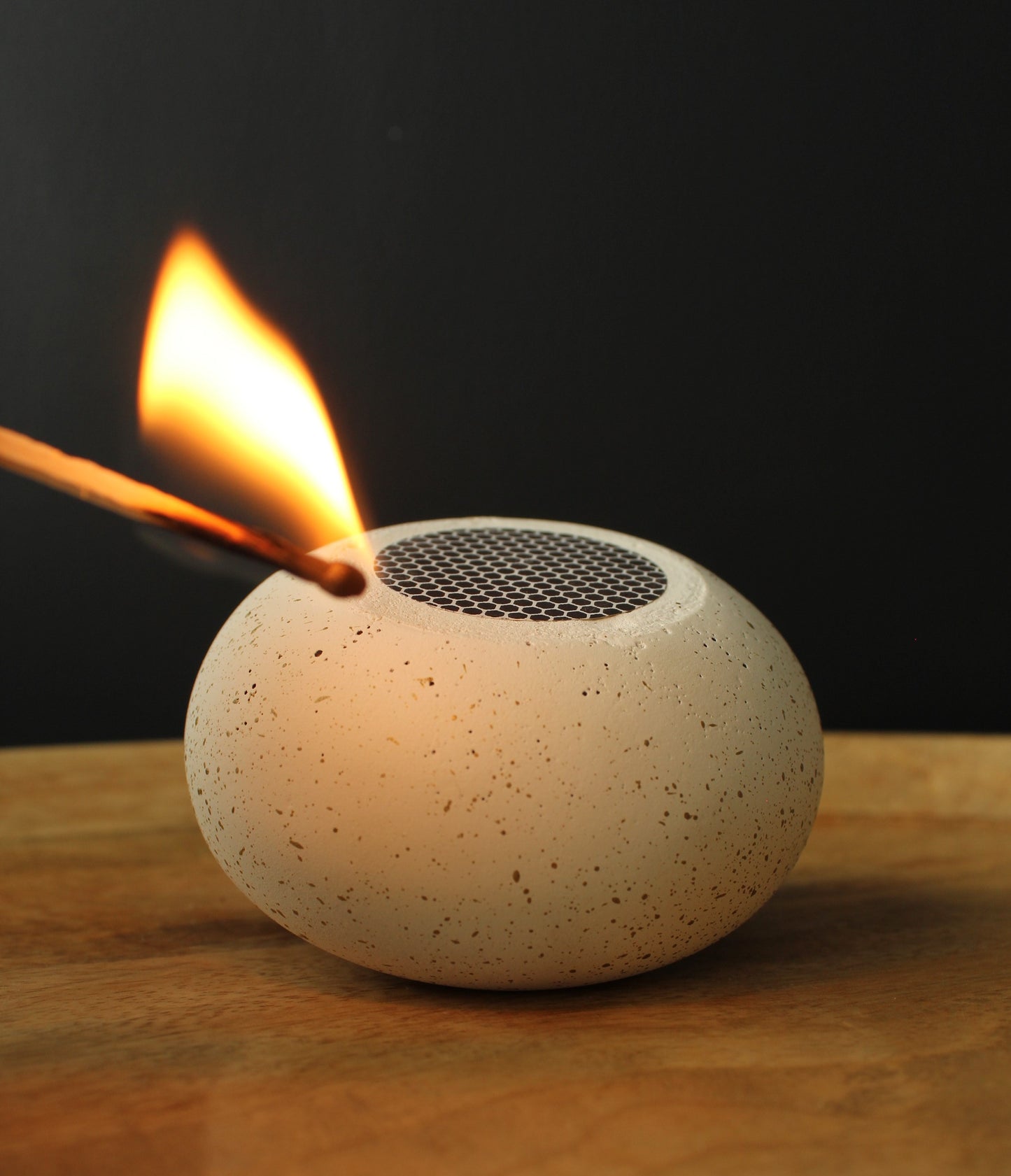 Speckled stone match bowl with match being ignited with a match on a wooden surface.
