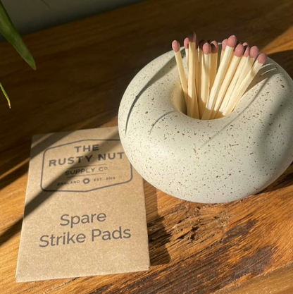 Matches in a stone holder with spare strike pads on a wooden surface