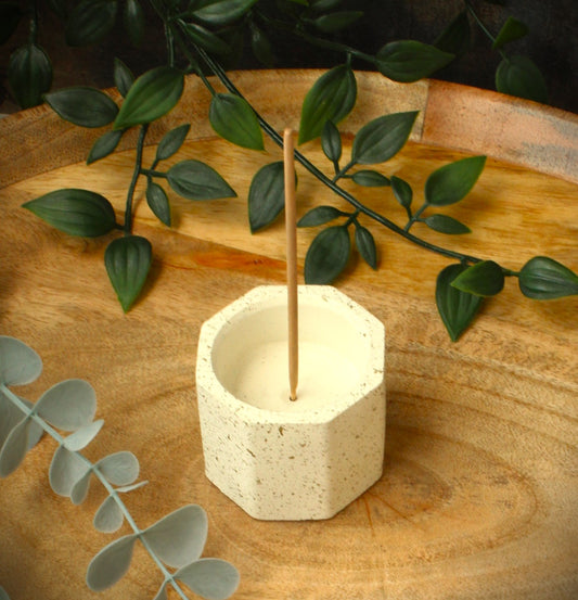 Handmade hexagonal cast stone incense holder in antique white with gold flecks, placed on a rustic wooden tray with botanical accents. Designed for Indian-style incense sticks, styled in a calm, natural setting.