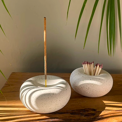 Stone incense holder and match bowl with a lit incense stick and matches on a wooden surface.