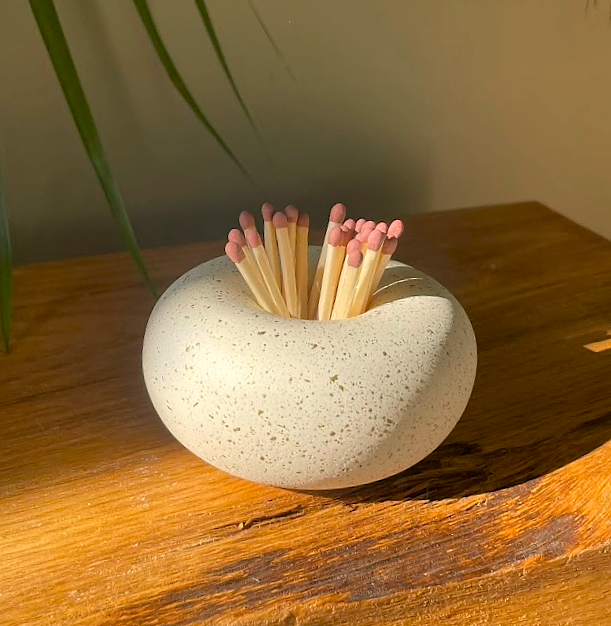 Matches in a stonebowl holder on a wooden surface with a plant in the background