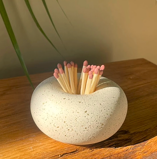 Matches in a stone holder on a wooden surface with a plant in the background