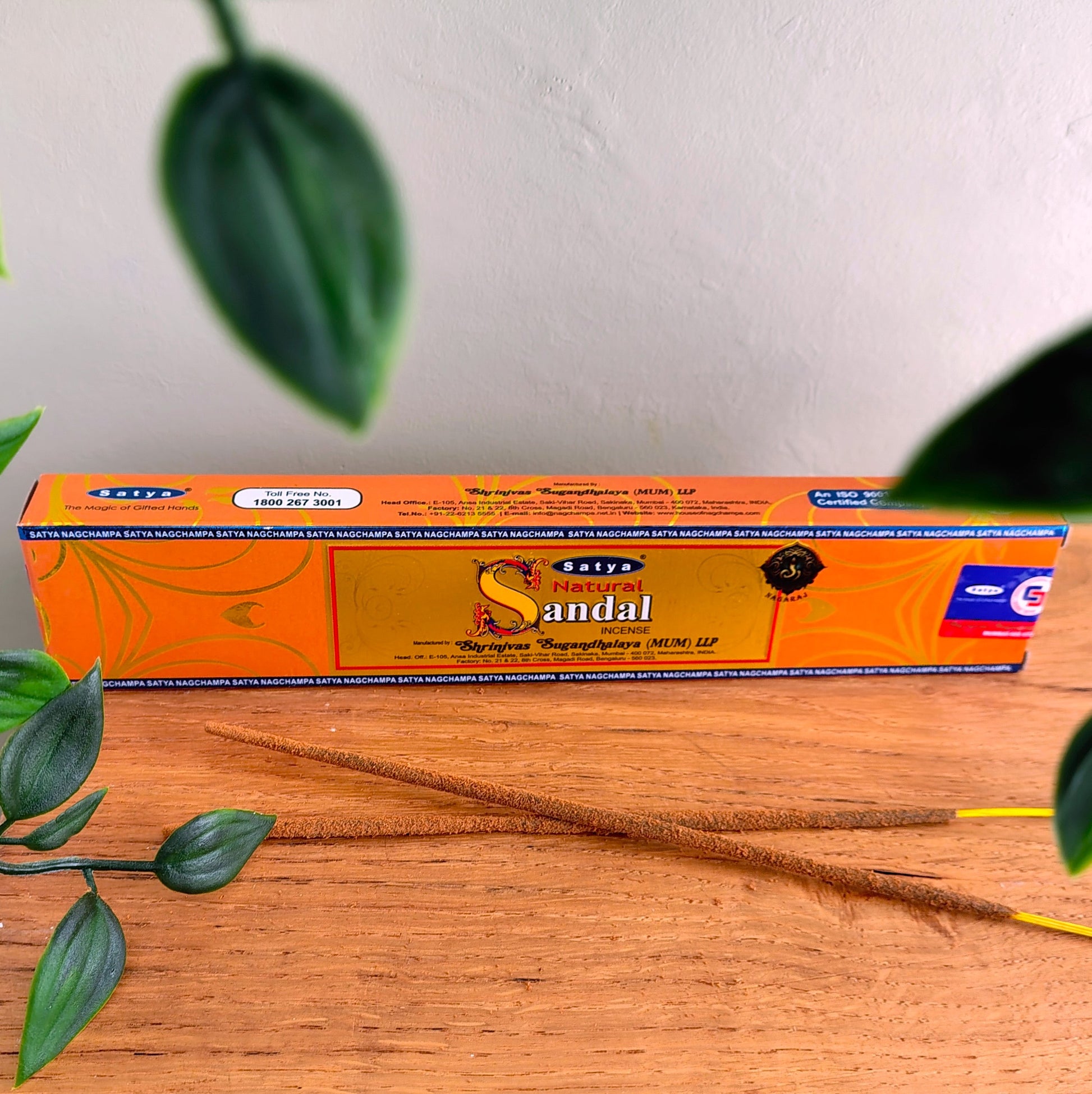 Satya Natural Sandal incense sticks box with two incense sticks laid in front, on a wooden table