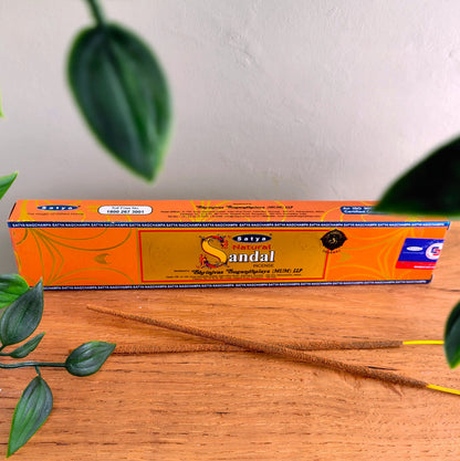 Satya Natural Sandal incense sticks box with two incense sticks laid in front, on a wooden table