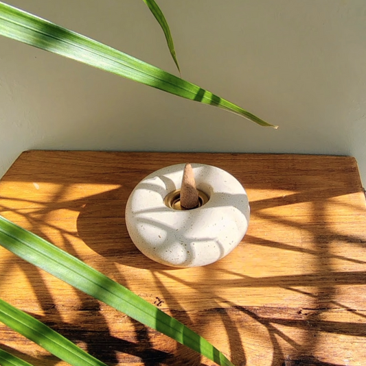 Stone incense cone dish on a wooden surface with green leaves