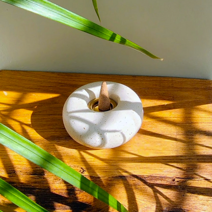 Antique white stone incense cone dish with a wooden stick on a wooden surface with green leaves.