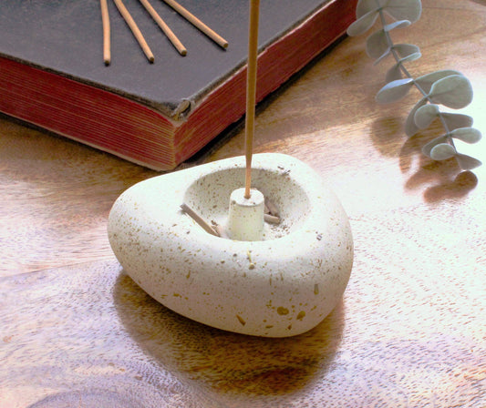 Antique white heart shaped incense stick holder sitting on a wooden surface with an old book in the background. 4 incense stick sit on the book