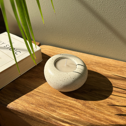 Cast stone Sanctuary tealight holder with lit tealight styled beside an open book, alternate angle