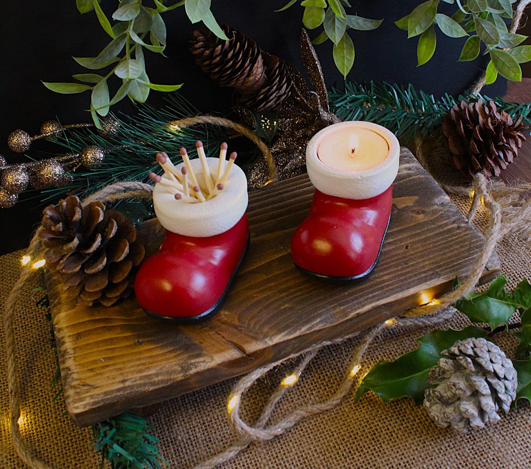 Santa boot set with matches and a lit tea light among pine cones