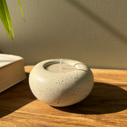 Cast stone Sanctuary tealight holder with lit tealight styled beside a stack of books on a wooden table